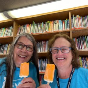 Two older women eating orange popsicles