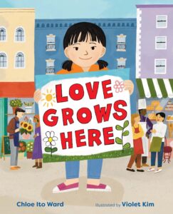 Girl with low pigtails holds sign that says "Love Grows Here" with buildings and people smiling behind her