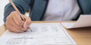 Student hand holding a pencil and taking a test at a desk.