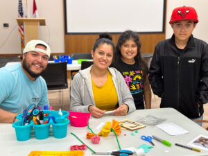 Family smiling as they decorate a frame to place a photo of their loved one for the library's community ofrenda. 
