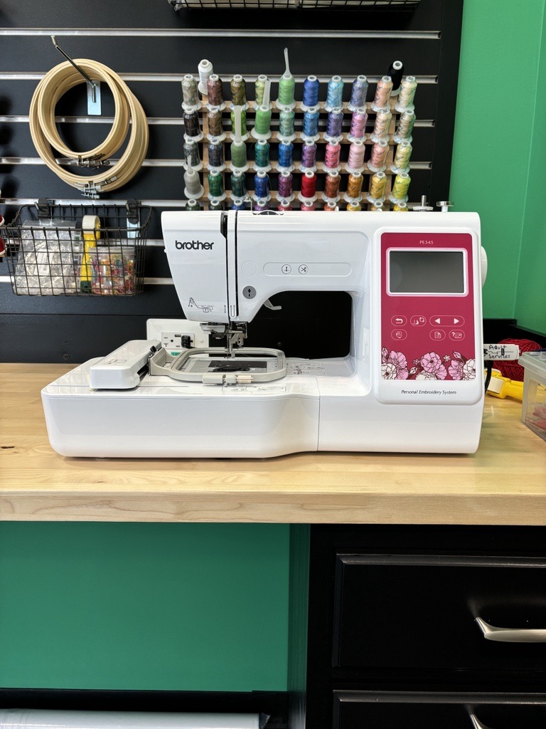 White embroidery machine sitting on a wooden table.