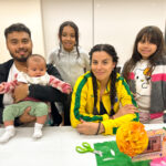Family smiling towards the camera as they decorate a picture frame for the library's community ofrenda.