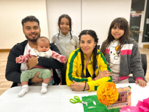 Family smiling towards the camera as they decorate a picture frame for the library's community ofrenda.