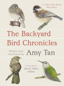The cover of “The Backyard Bird Chronicles” by Amy Tan. Four drawn birds frame the cover. Each bird is perched on its own respective branch. There is a beige background and the title is in red in the center of the cover.