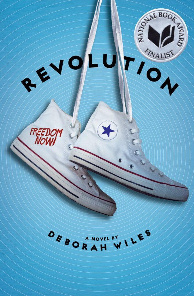 An image of the book cover for “Revolution” by Deborah Wiles. A pair of high top Converse shoes dangle by the laces in front of a blue background.