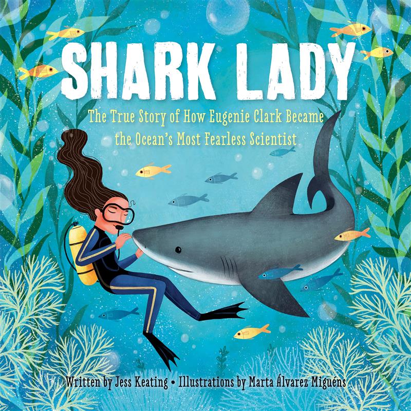 An image of the book cover for “Shark Lady” by Jess Keating. A drawn depiction of a female diver underwater. Her hands hover around the nose of a shark. They are surrounded by underwater plant life and small golden fish. 